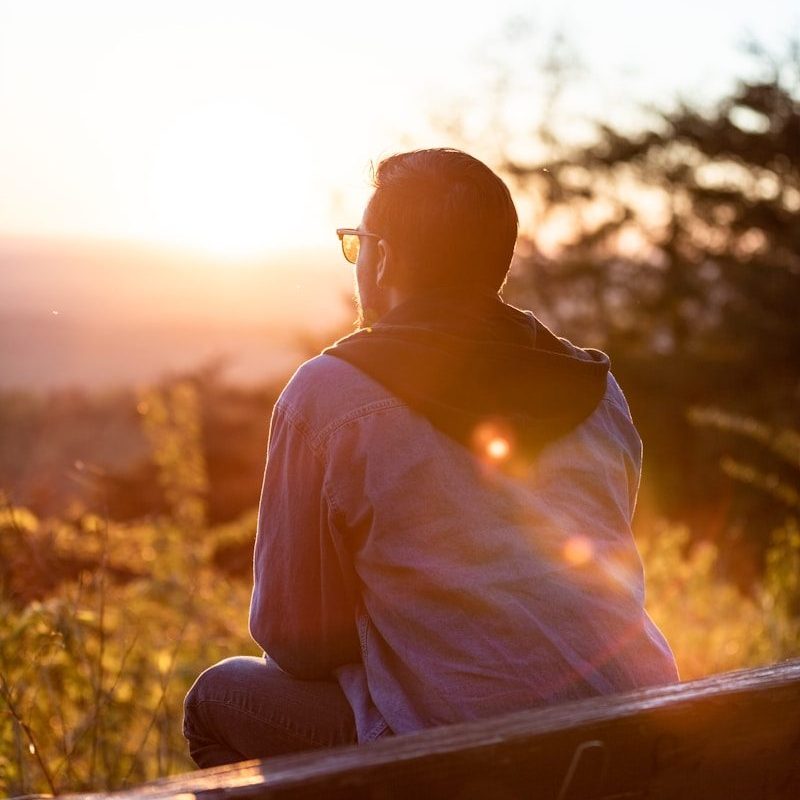 woman in white shirt and sunglasses sitting on brown wooden bench during sunset
